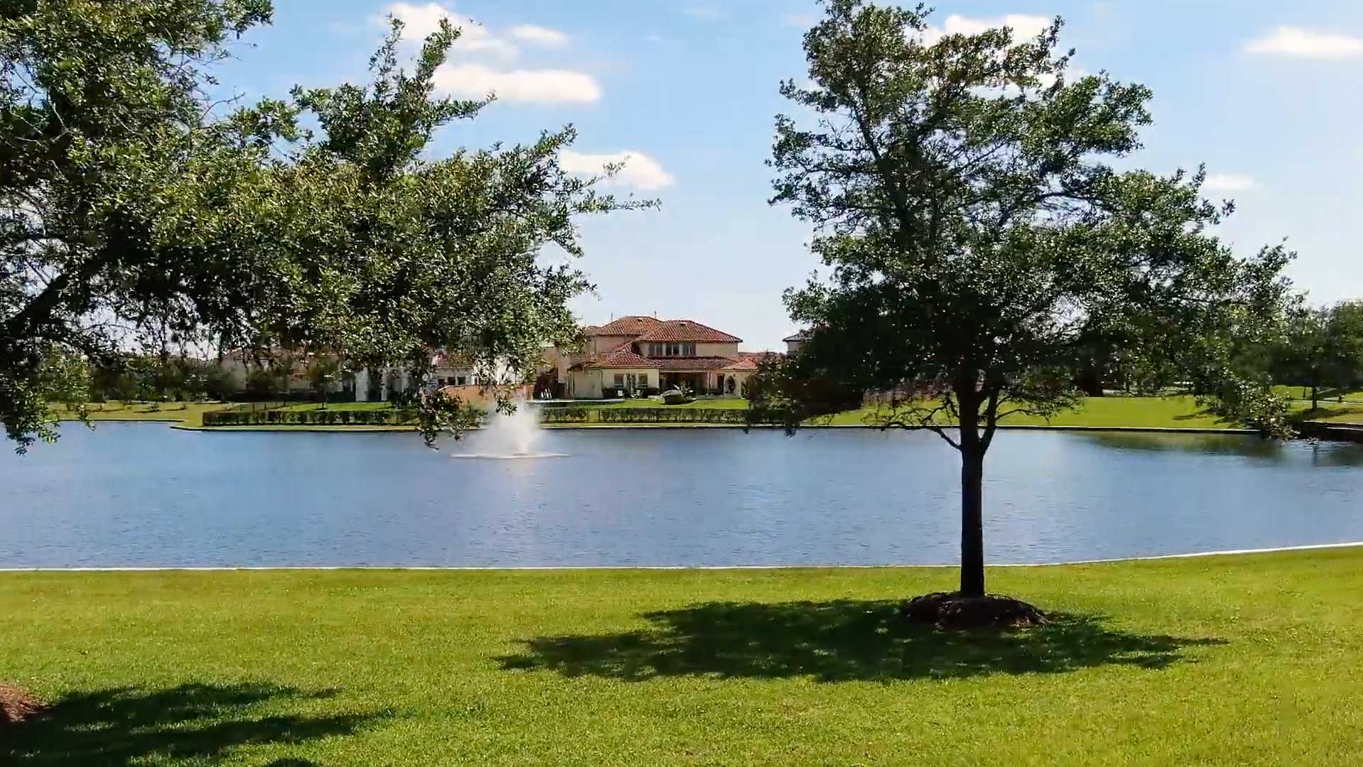 Ground-level view of a fountained lake framed by oak trees at Tuscan Lakes